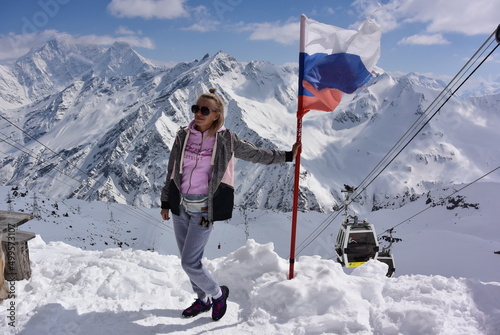 Young girl on the background of snow-capped mountains and the flag of Russia. Elbrus April 25, 2019