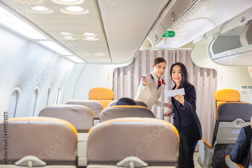 Happy Asian woman traveler standing and holding boarding pass while Flight attendant is checking passenger boarding pass in business class and show the way to her seat for airplane flight. Copy space