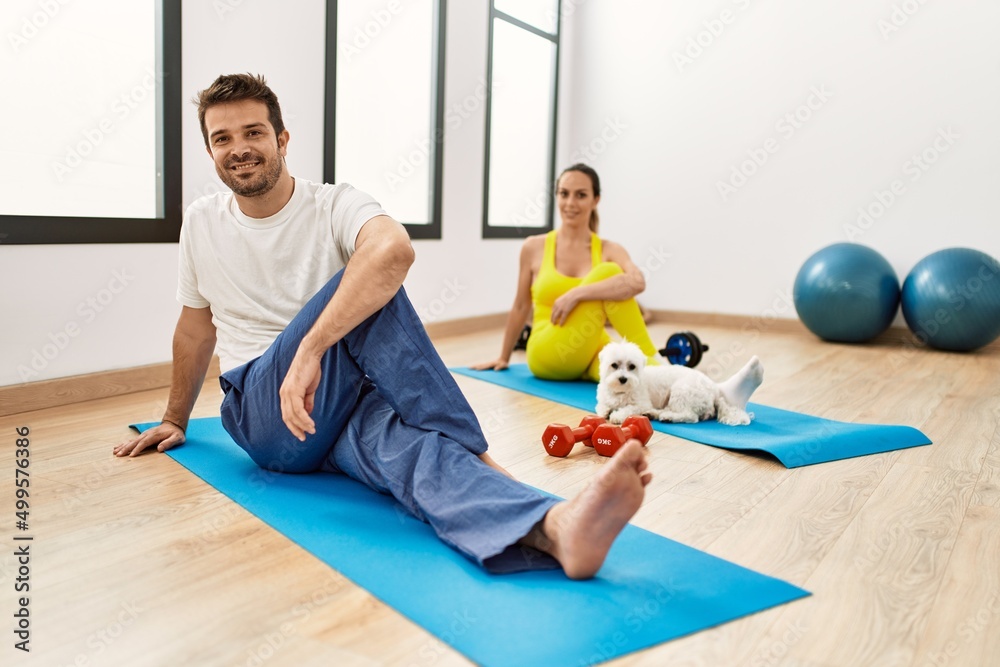 Young hispanic sporty couple stretching sitting on yoga mat at sport center.