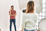 Woman photographer talking pictures of man posing as model at photography studio smiling with happy face winking at the camera doing victory sign. number two.