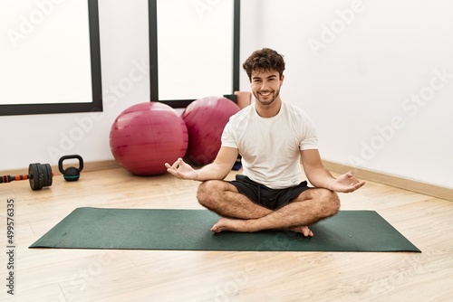 Young hispanic man smiling confident training yoga exercise at sport center