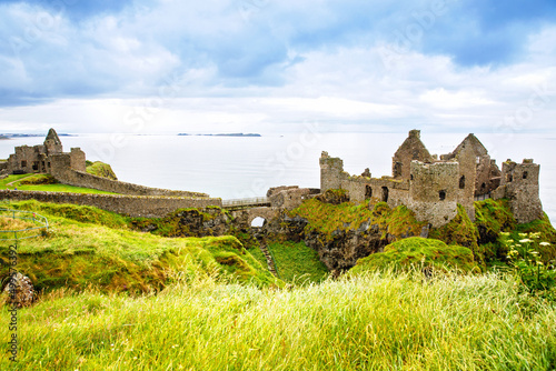 Ruins of Dunluce Castle, Antrim, Northern Ireland during sunny day with semi cloudy sky. Irish ancient castle near Wild Atlantic Way. photo