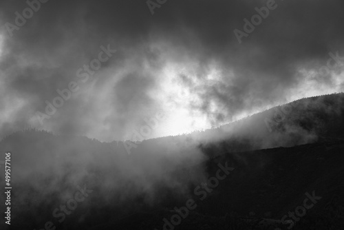 a black and white picture taken from the mountain down through the clouds to the shining atlantic ocean. Madeira, Portugal