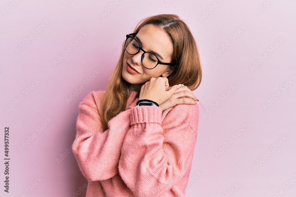 Young blonde woman wearing casual clothes and glasses hugging oneself happy and positive, smiling confident. self love and self care