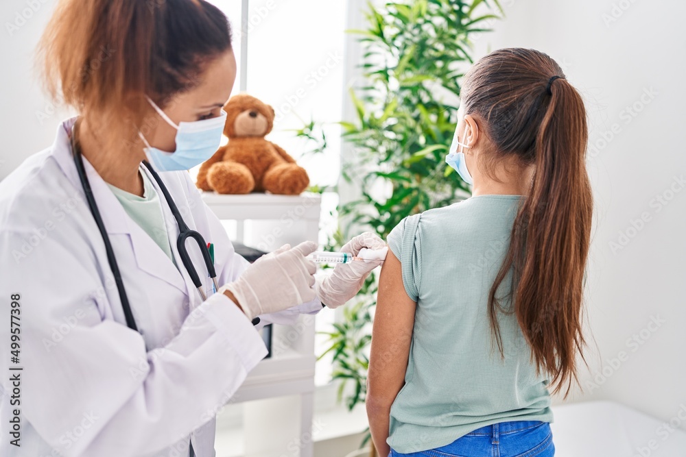 Woman and girl doctor and patient wearing medical mask vaccinating arm at clinic Woman and girl doctor and patient wearing medical mask vaccinating arm at clinic