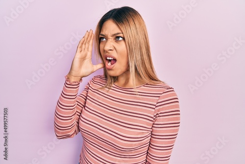 Beautiful hispanic woman wearing casual striped sweater shouting and screaming loud to side with hand on mouth. communication concept.