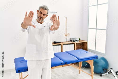 Middle age hispanic therapist man working at pain recovery clinic doing frame using hands palms and fingers, camera perspective