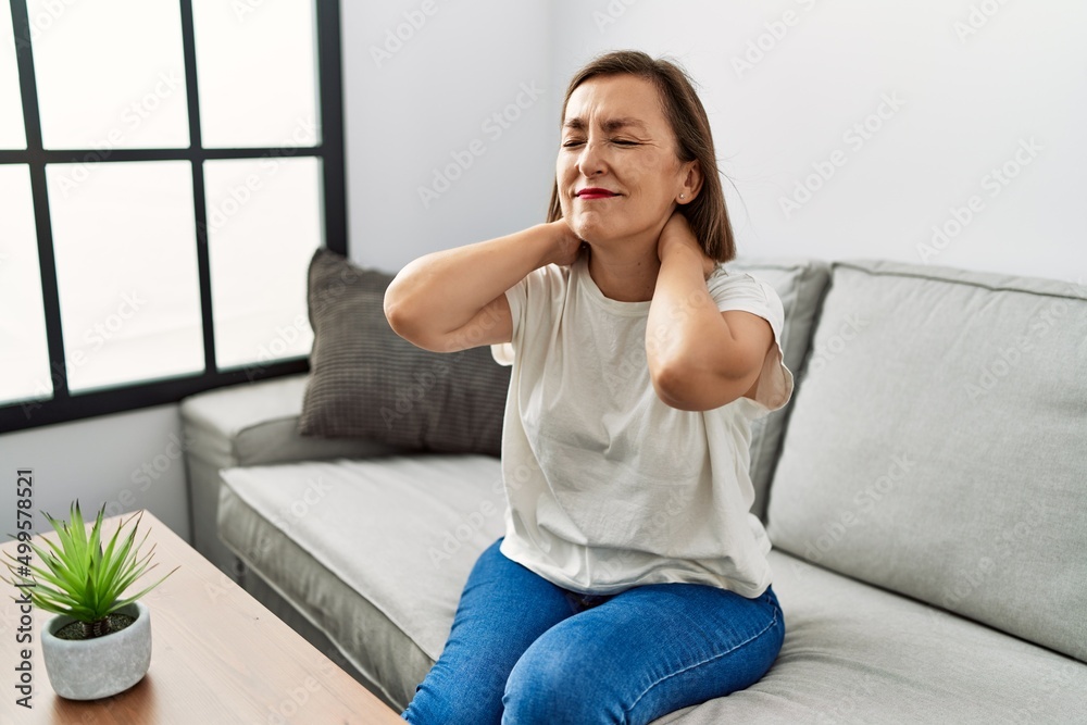 Middle age hispanic woman sitting on the sofa with neck pain at home Middle age hispanic woman sitting on the sofa with neck pain at home