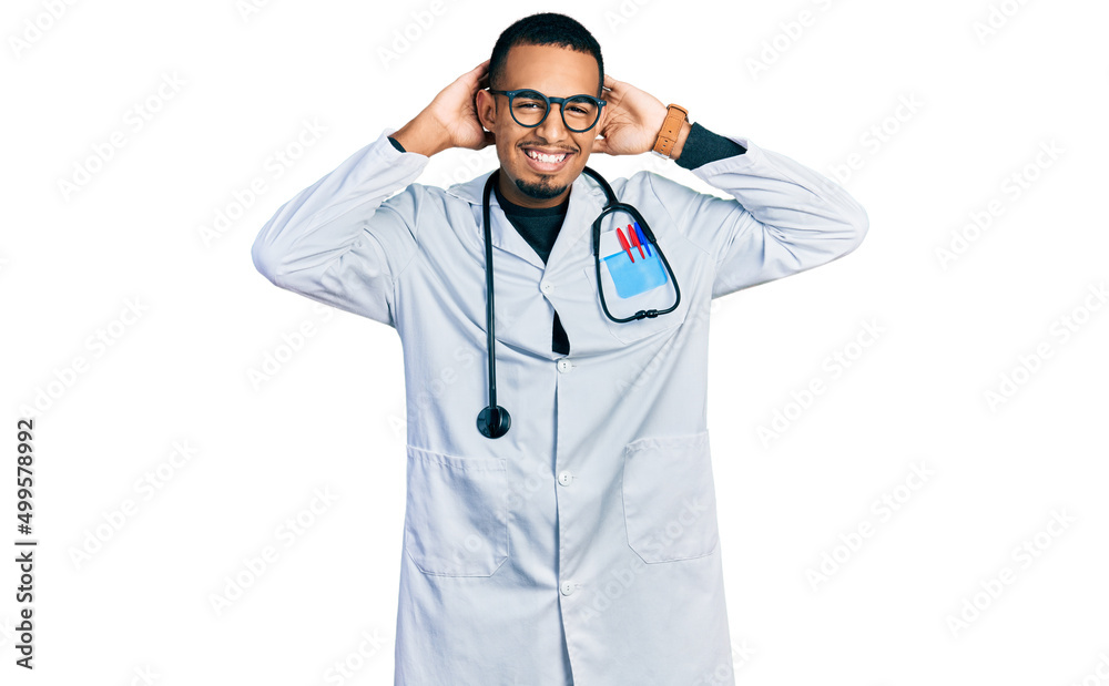 Young african american man wearing doctor uniform and stethoscope relaxing and stretching, arms and hands behind head and neck smiling happy Young african american man wearing doctor uniform and stethoscope relaxing and stretching, arms and hands behind head and neck smiling happy