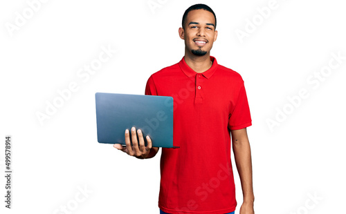 Young african american man working using computer laptop looking positive and happy standing and smiling with a confident smile showing teeth