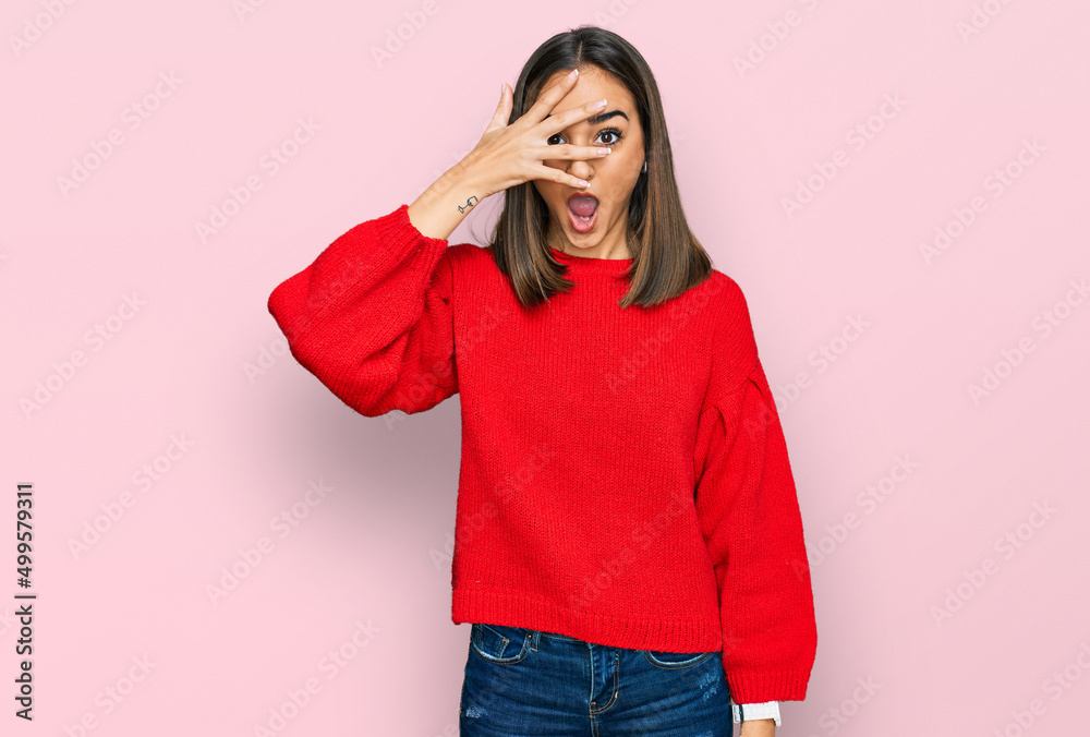 Beautiful brunette woman wearing casual winter sweater peeking in shock covering face and eyes with hand, looking through fingers with embarrassed expression. Beautiful brunette woman wearing casual winter sweater peeking in shock covering face and eyes with hand, looking through fingers with embarrassed expression.