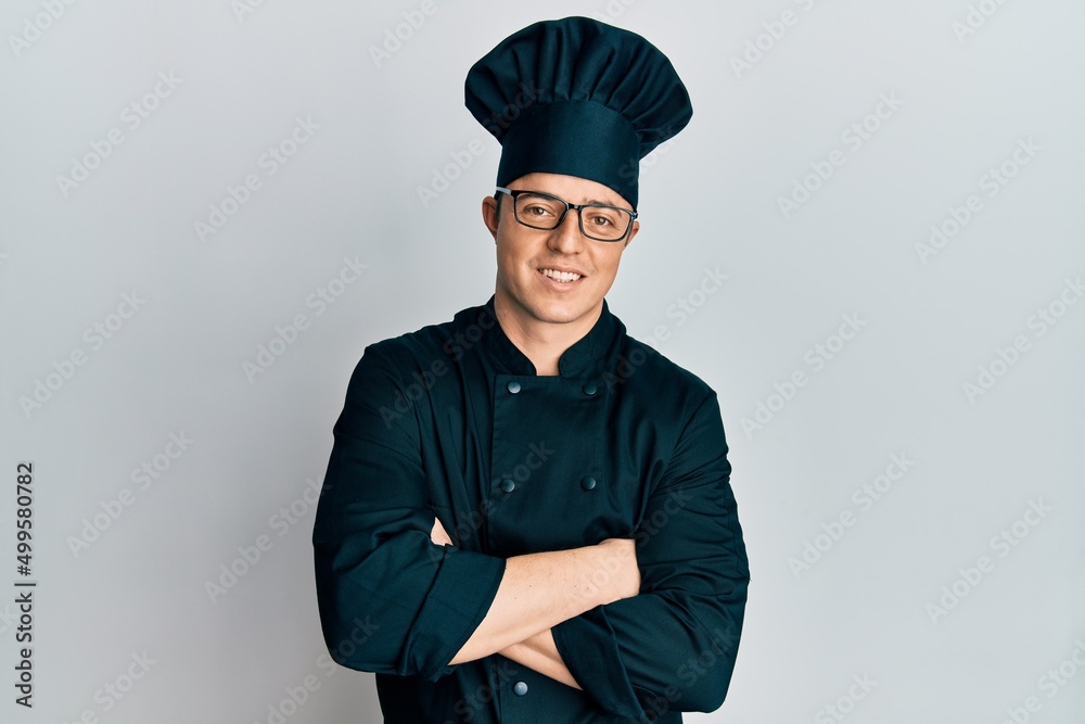 Handsome young man wearing professional cook uniform and hat happy face smiling with crossed arms looking at the camera. positive person. Handsome young man wearing professional cook uniform and hat happy face smiling with crossed arms looking at the camera. positive person.
