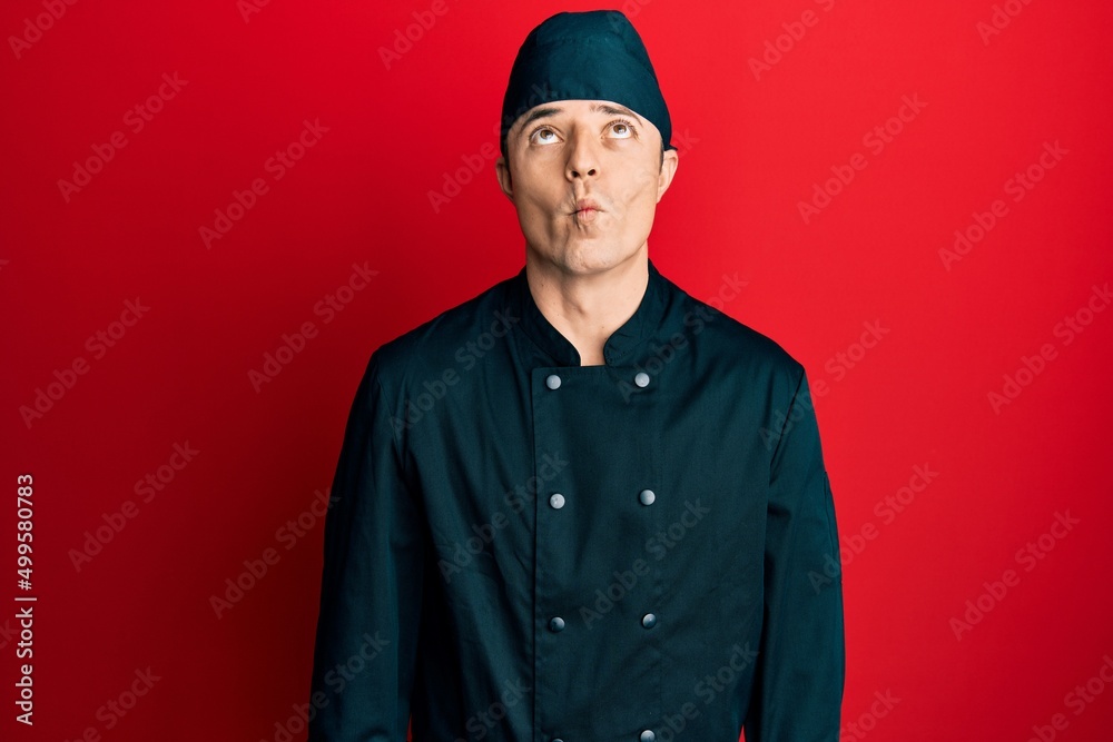 Handsome young man wearing professional cook uniform and hat making fish face with lips, crazy and comical gesture. funny expression. Handsome young man wearing professional cook uniform and hat making fish face with lips, crazy and comical gesture. funny expression.