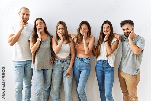 Group of young friends standing together over isolated background touching mouth with hand with painful expression because of toothache or dental illness on teeth. dentist concept.