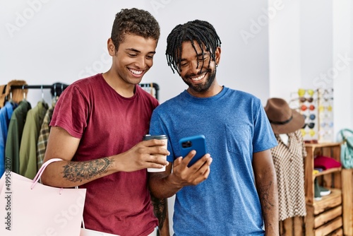 Two men friends holding shopping bags using smartphone at clothing store
