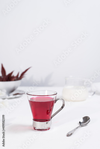Una taza transparente de t   de bayas y leche sobre una mesa blanca.
