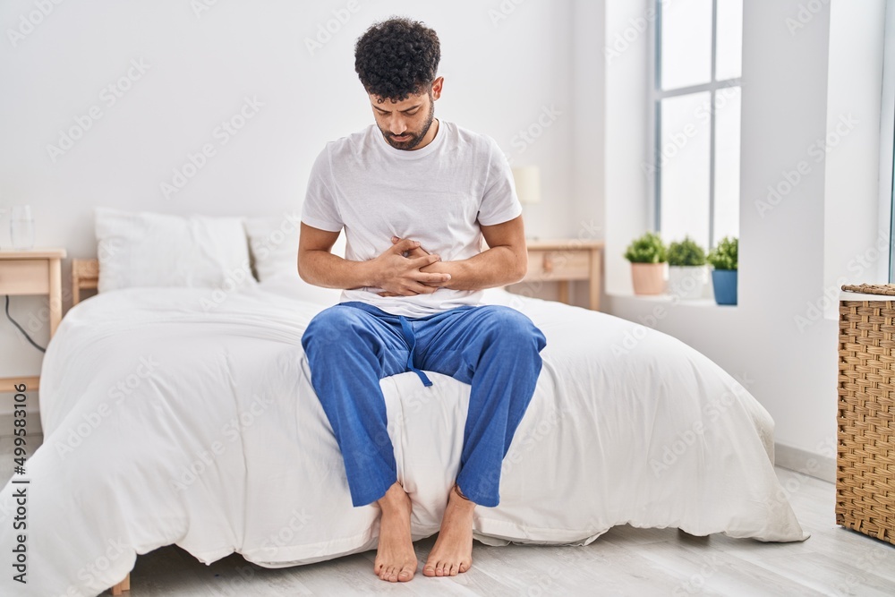 Young arab man suffering for stomachache sitting on bed at bedroom Young arab man suffering for stomachache sitting on bed at bedroom
