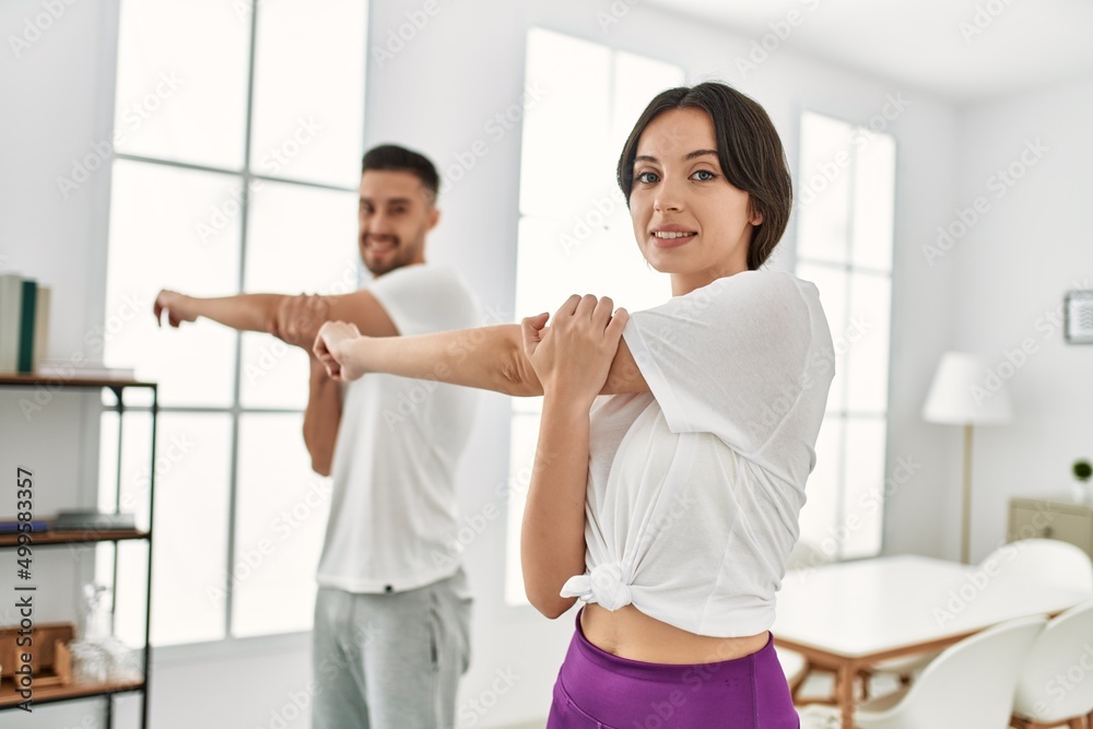 Fototapeta premium Young hispanic couple doing sport streching arms at home