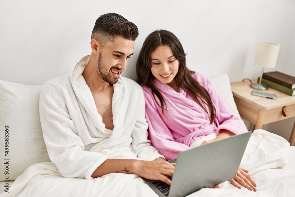 Young hispanic couple using laptop lying in bed at home. Young hispanic couple using laptop lying in bed at home.