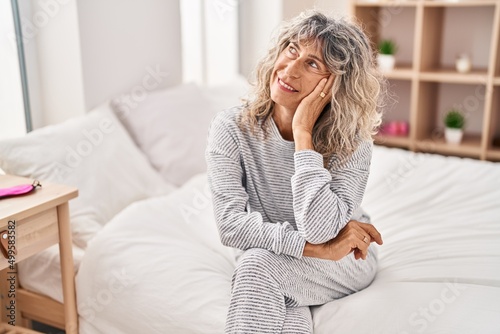 Middle age woman smiling confident sitting on bed at bedroom