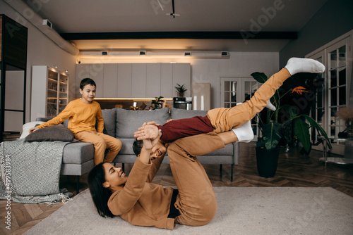 Mom teaches her two sons to do sports physical exercises in the morning at home