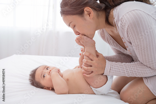 Happy loving family. Baby feet in mother hands. asian mother lifting and playing with baby in the bedroom, asia mother hug cuddle little infant or toddler, enjoy tender family moment, motherhood.