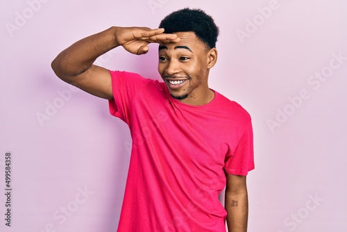 Young african american man wearing casua t shirt very happy and smiling looking far away with hand over head. searching concept.