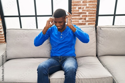 Young african american man listening to music sitting on sofa at home
