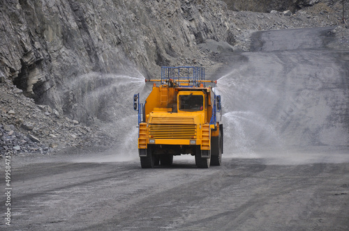Heavy truck pours the road with water in the iron ore quarry. Dust removal, protection of the environment. Irrigation of the road from dust