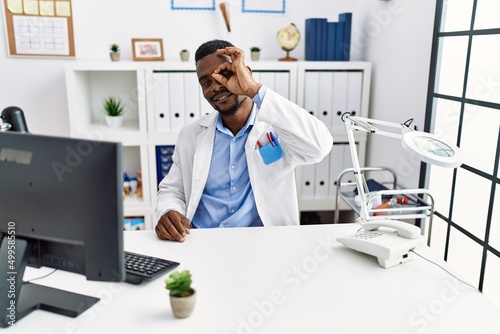 Young african doctor man wearing stethoscope at the clinic smiling happy doing ok sign with hand on eye looking through fingers