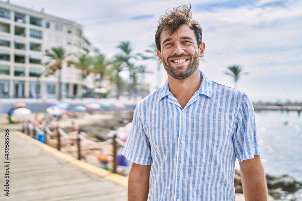 Fototapeta premium Young hispanic man smiling happy standing at the beach.