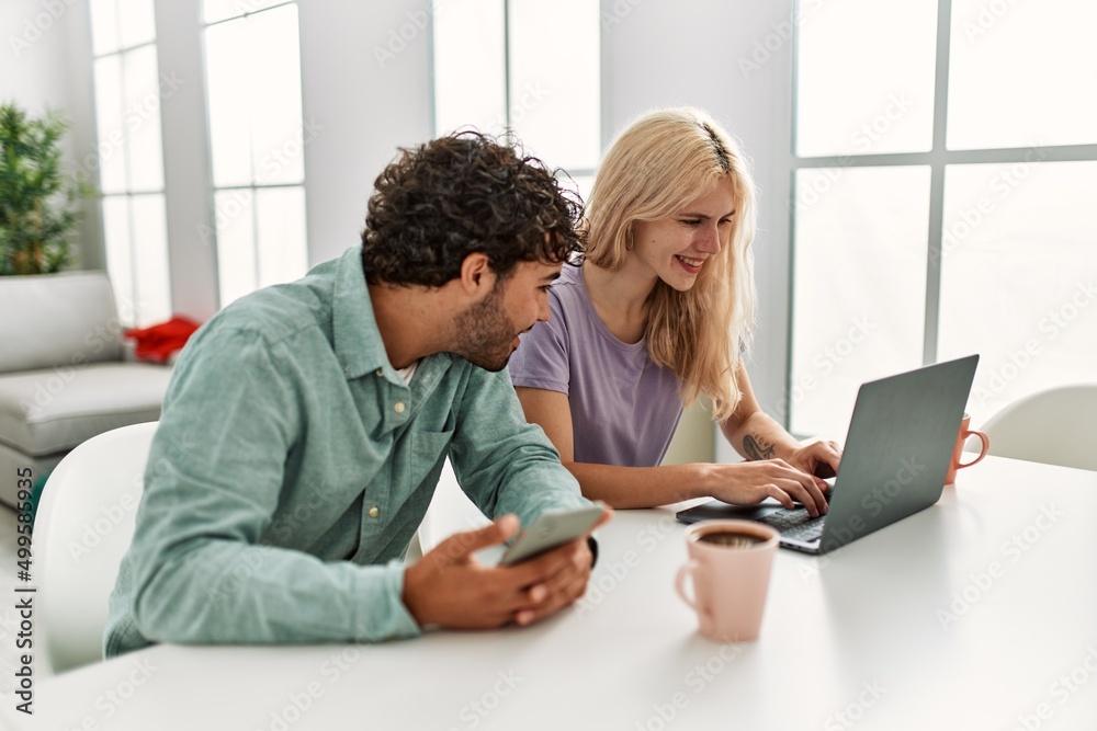 Young couple using laptop and smartphone drinking coffee at home. Young couple using laptop and smartphone drinking coffee at home.