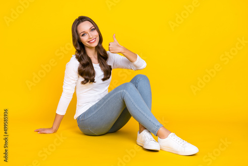 Fototapeta Naklejka Na Ścianę i Meble -  Photo of charming sweet lady dressed white shirt sitting floor showing thumb up isolated yellow color background