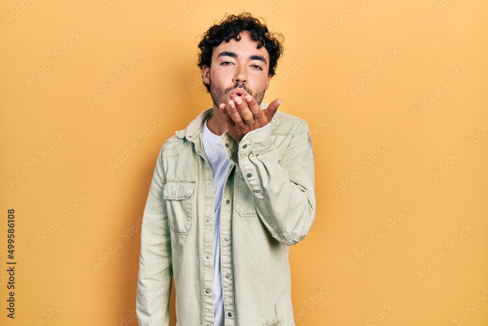 Young hispanic man wearing casual clothes looking at the camera blowing a kiss with hand on air being lovely and sexy. love expression. Young hispanic man wearing casual clothes looking at the camera blowing a kiss with hand on air being lovely and sexy. love expression.