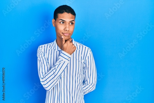 Young african american guy wearing casual clothes with hand on chin thinking about question, pensive expression. smiling with thoughtful face. doubt concept.