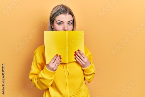 Beautiful caucasian woman holding open book relaxed with serious expression on face. simple and natural looking at the camera.