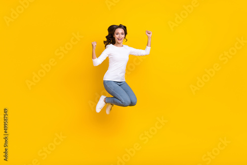 Photo of sweet lucky woman wear white shirt rising fists jumping high isolated yellow color background © deagreez