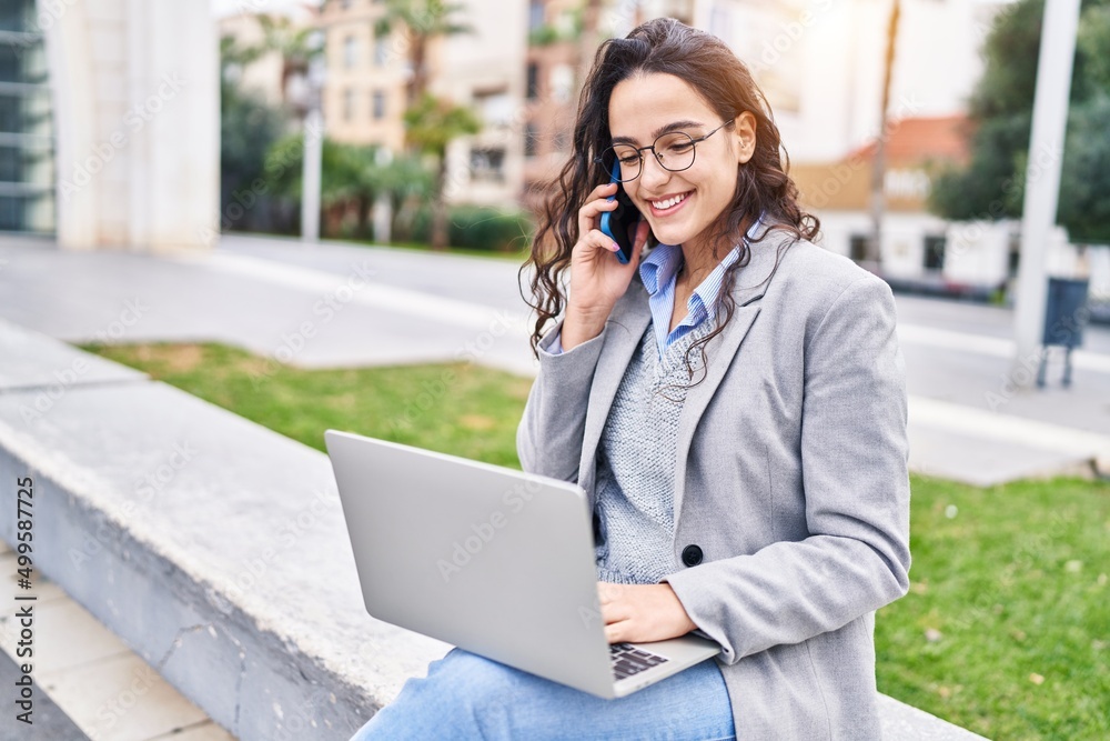 Young hispanic woman executive using laptop and talking on the smartphone at street Young hispanic woman executive using laptop and talking on the smartphone at street