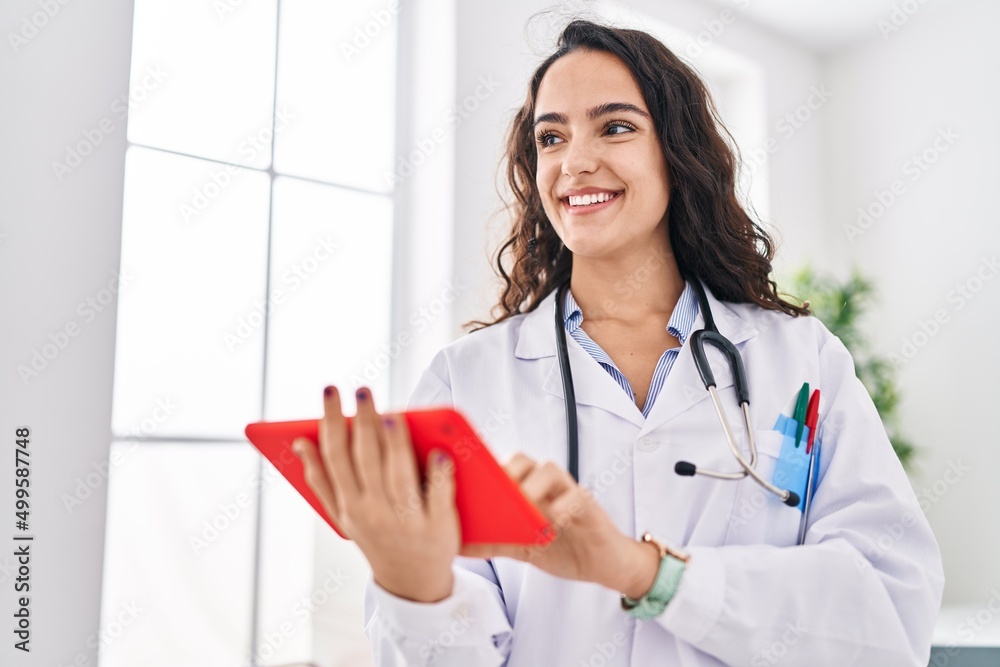 Young hispanic woman wearing doctor uniform using touchpad at clinic Young hispanic woman wearing doctor uniform using touchpad at clinic