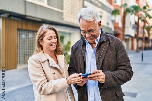 Middle age man and woman couple smiling confident using smartphone at street