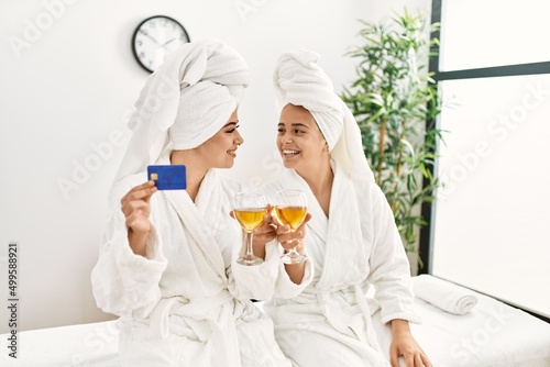 Woman couple holding credit card and toasting with champagne sitting on massage board at beauty center photo