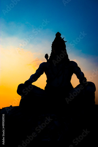 back lit statue of hindu god lord shiva in meditation posture with dramatic sky from unique angle