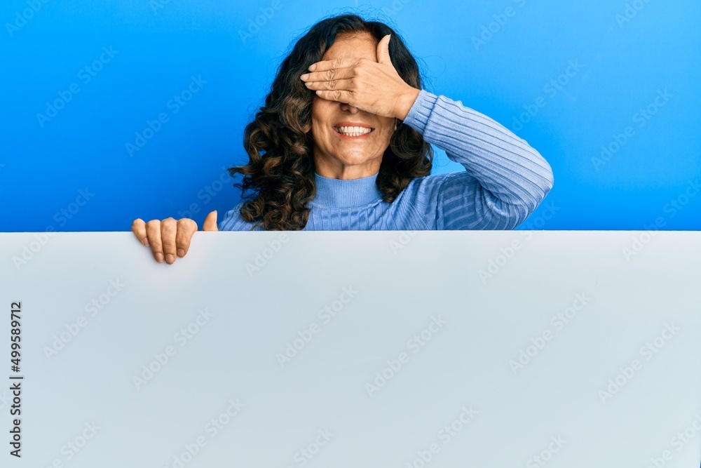 Middle age hispanic woman holding blank empty banner smiling and laughing with hand on face covering eyes for surprise. blind concept. Middle age hispanic woman holding blank empty banner smiling and laughing with hand on face covering eyes for surprise. blind concept.