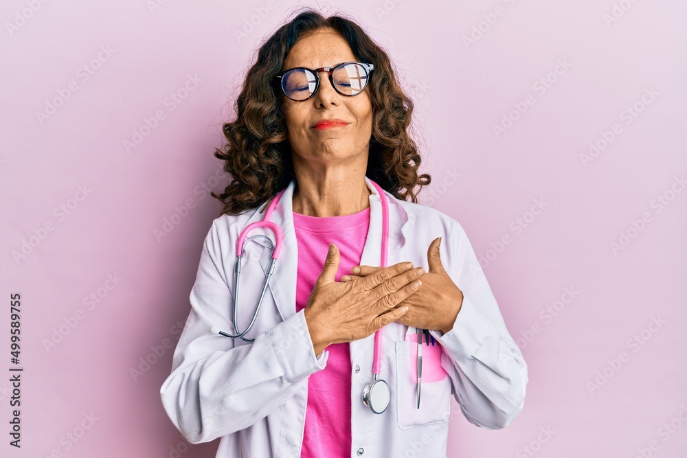 Middle age hispanic woman wearing doctor uniform and glasses smiling with hands on chest with closed eyes and grateful gesture on face. health concept.