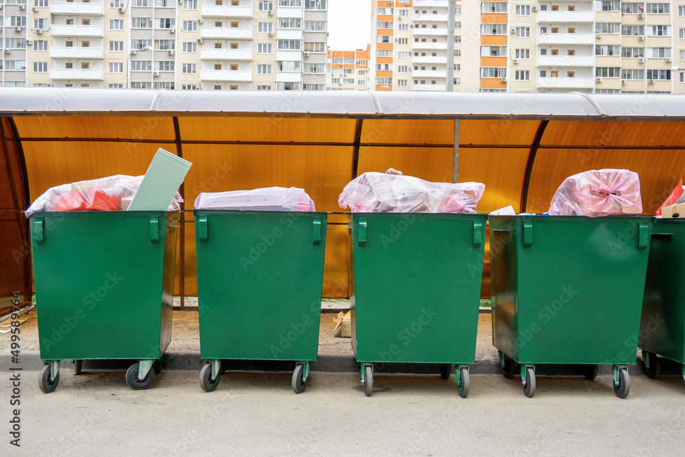 Row of green overfill garbage bins in residential, front view. Trash in dustbins on city street. Row of green overfill garbage bins in residential, front view. Trash in dustbins on city street.