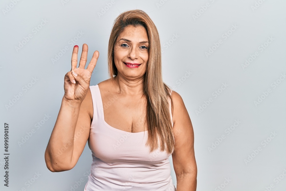 Middle age hispanic woman wearing casual style with sleeveless shirt showing and pointing up with fingers number three while smiling confident and happy. Middle age hispanic woman wearing casual style with sleeveless shirt showing and pointing up with fingers number three while smiling confident and happy.