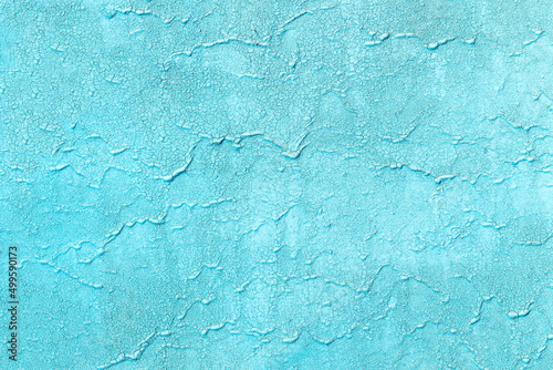 Texture of old painted azure wall with cracks. Rough blue background with scratches and paint smudges.