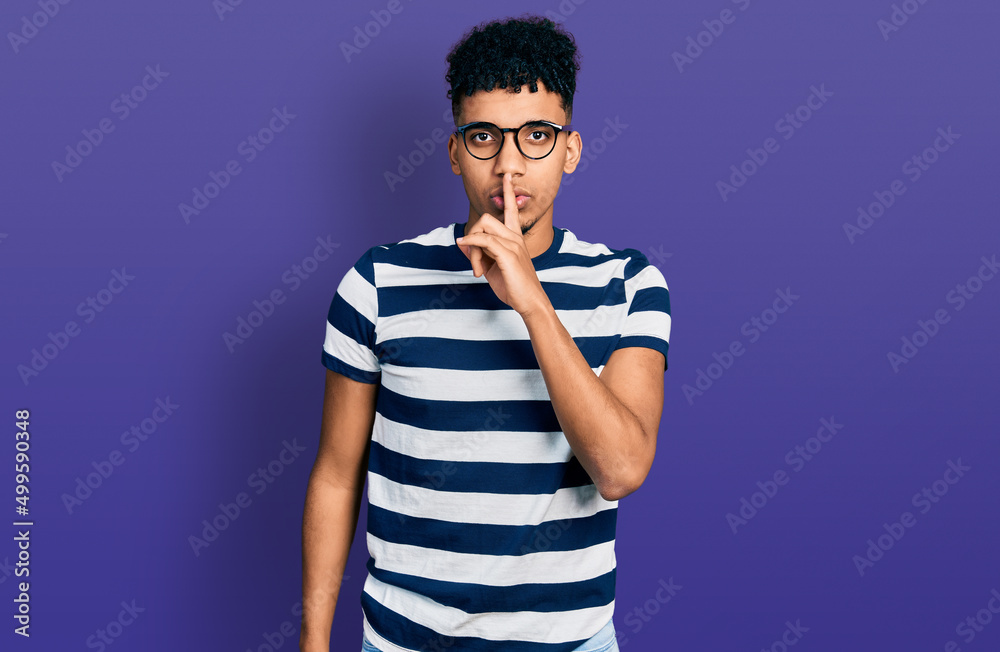 Young african american man wearing casual clothes and glasses asking to be quiet with finger on lips. silence and secret concept. Young african american man wearing casual clothes and glasses asking to be quiet with finger on lips. silence and secret concept.