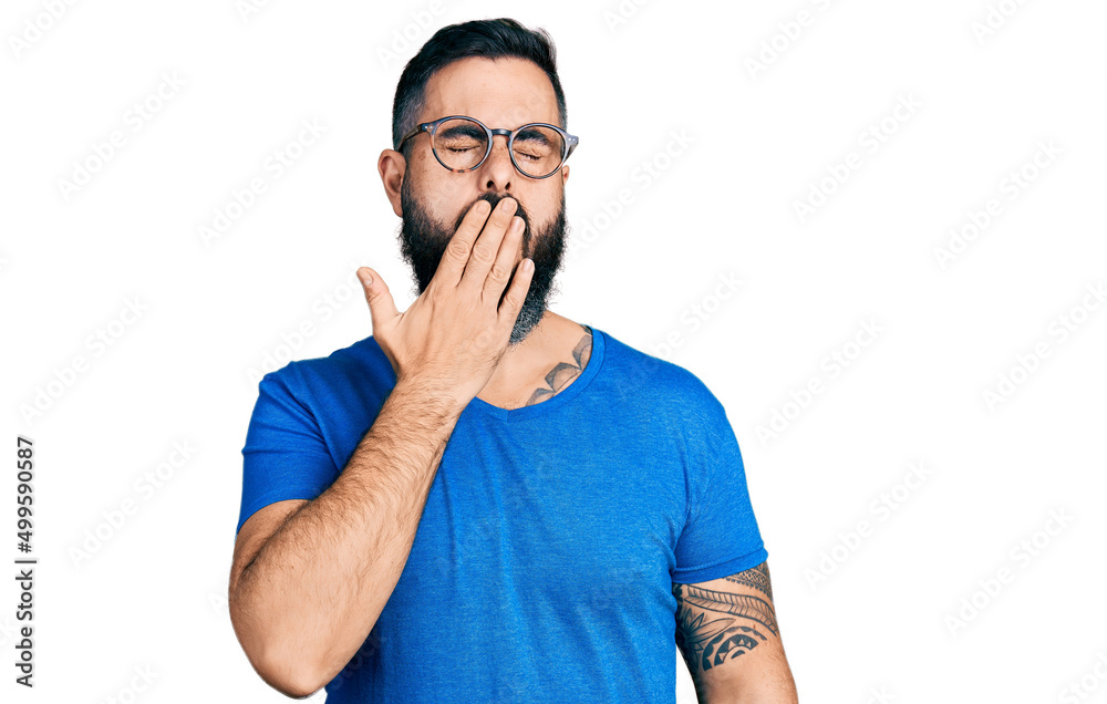 Hispanic man with beard wearing casual t shirt and glasses bored yawning tired covering mouth with hand. restless and sleepiness. Hispanic man with beard wearing casual t shirt and glasses bored yawning tired covering mouth with hand. restless and sleepiness.