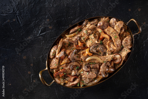 Mushroom beef stroganoff, a casserole of boletus, champignons, and meat, with cream sauce, shot from the top on a dark background with copy space